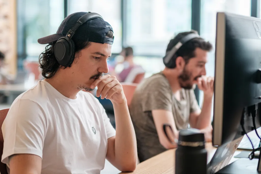 A male developer working at the Atolye15 İzmir office, wearing a white t-shirt, a black hat, and headphones.