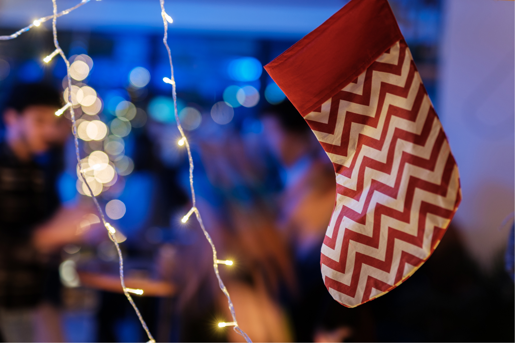 A red and white Christmas stocking and string lights in front of a blurred party background.