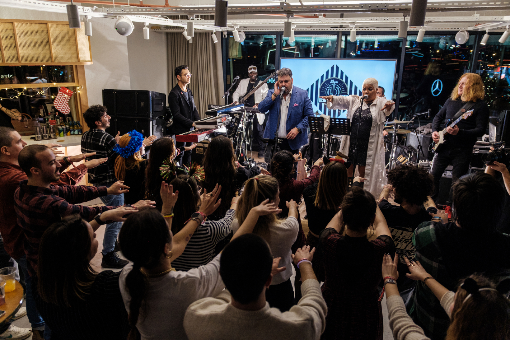 A group of people dancing with their hands up in the air in front of a music band at Atolye15’s new year office party.