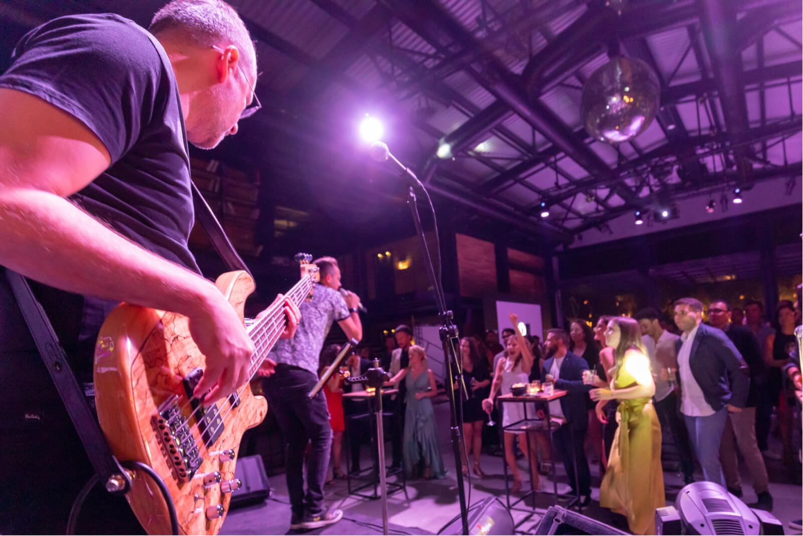 A man playing the electric guitar and a singer holding a microphone in front of a party crowd.