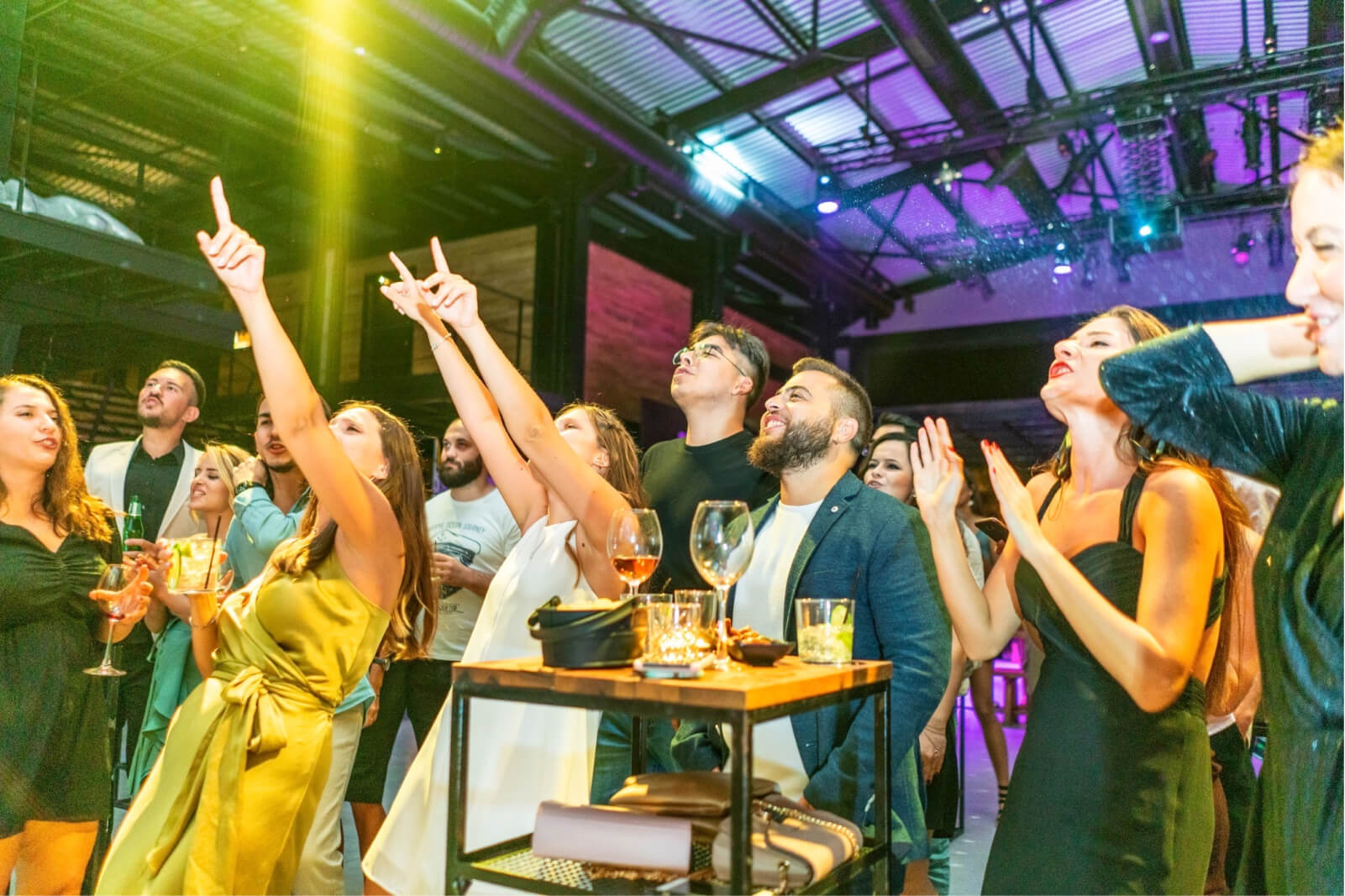 The Atolye15 Team at 10th-anniversary party, holding wine glasses, clapping, and singing with their hands in the air.