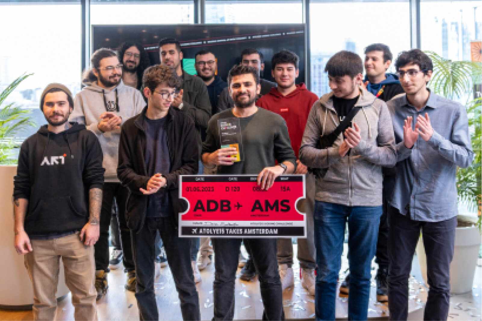 A group of young men gathered around the winner of Atolye15 Coding Challenge holding an award and a plane ticket to Amsterdam.