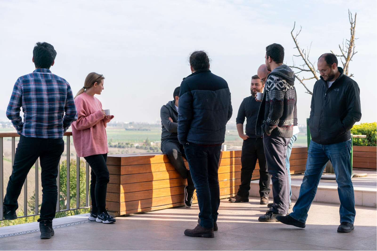 A group of people, walking around and having a conversation with one another while drinking coffee outside.