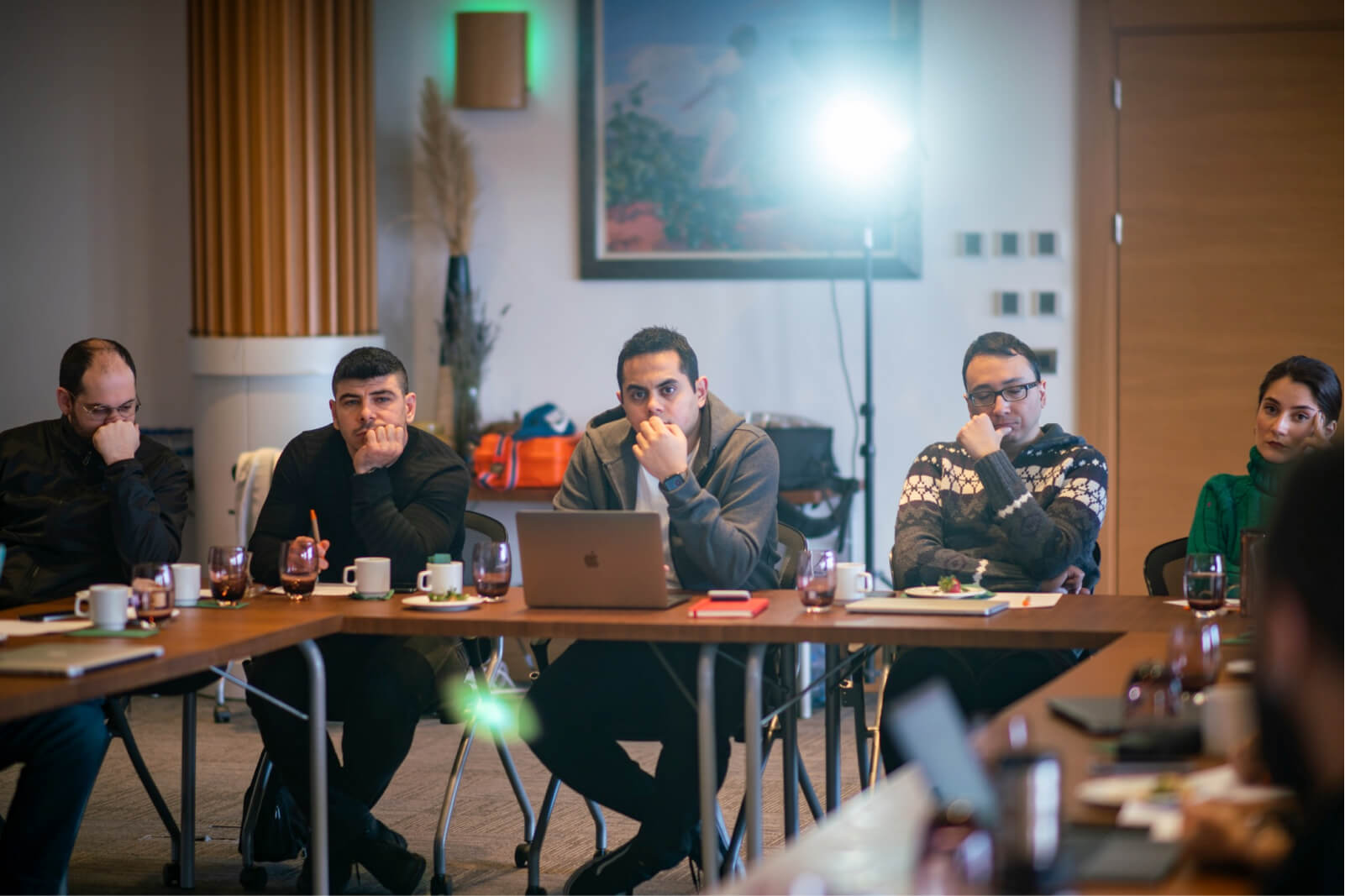 People sitting around a table in front of a laptop and thinking with their hands on their chin.