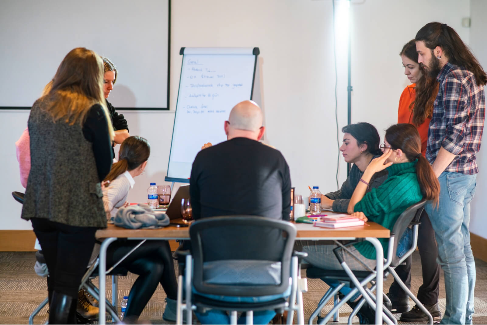 People sitting around a table and thinking looking at the writings on a whiteboard.