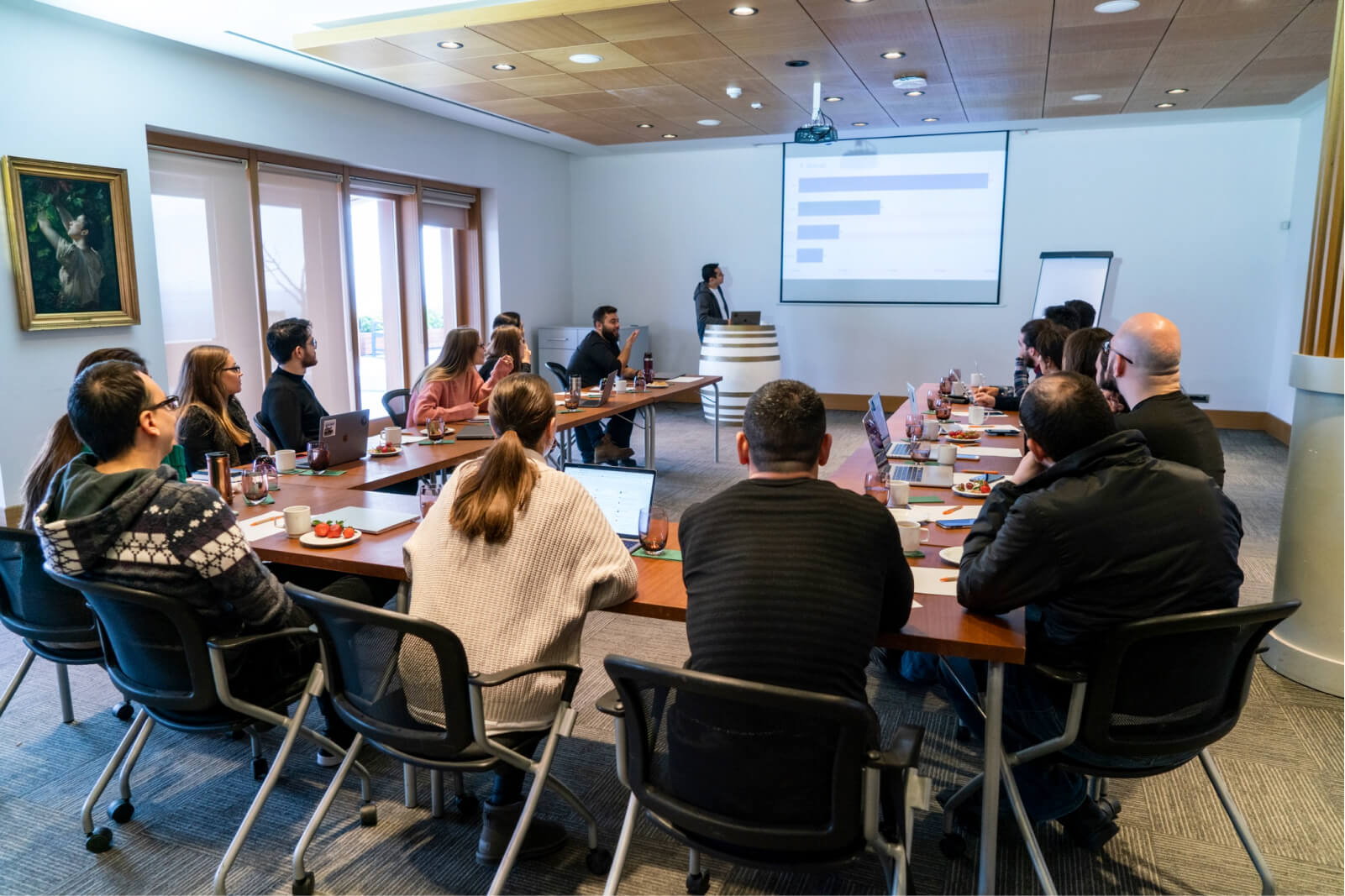 A group of people sitting around a table at a meeting looking at a projection on the wall.