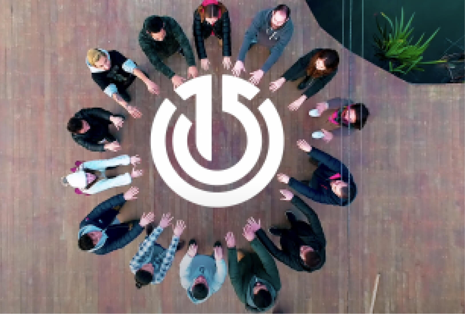 14 people gathered as a circle, posing with their arms stretched around the Atolye15 logo.
