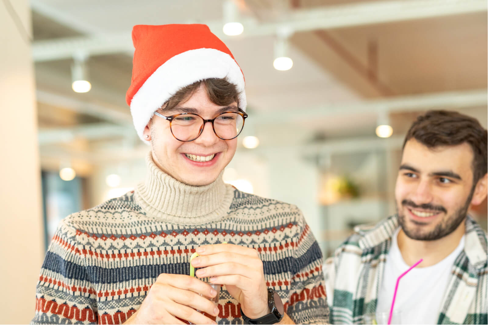 A young boy in a sweater, smiling, and wearing round glasses and a red Santa hat next to a bearded man in a plaid shirt.