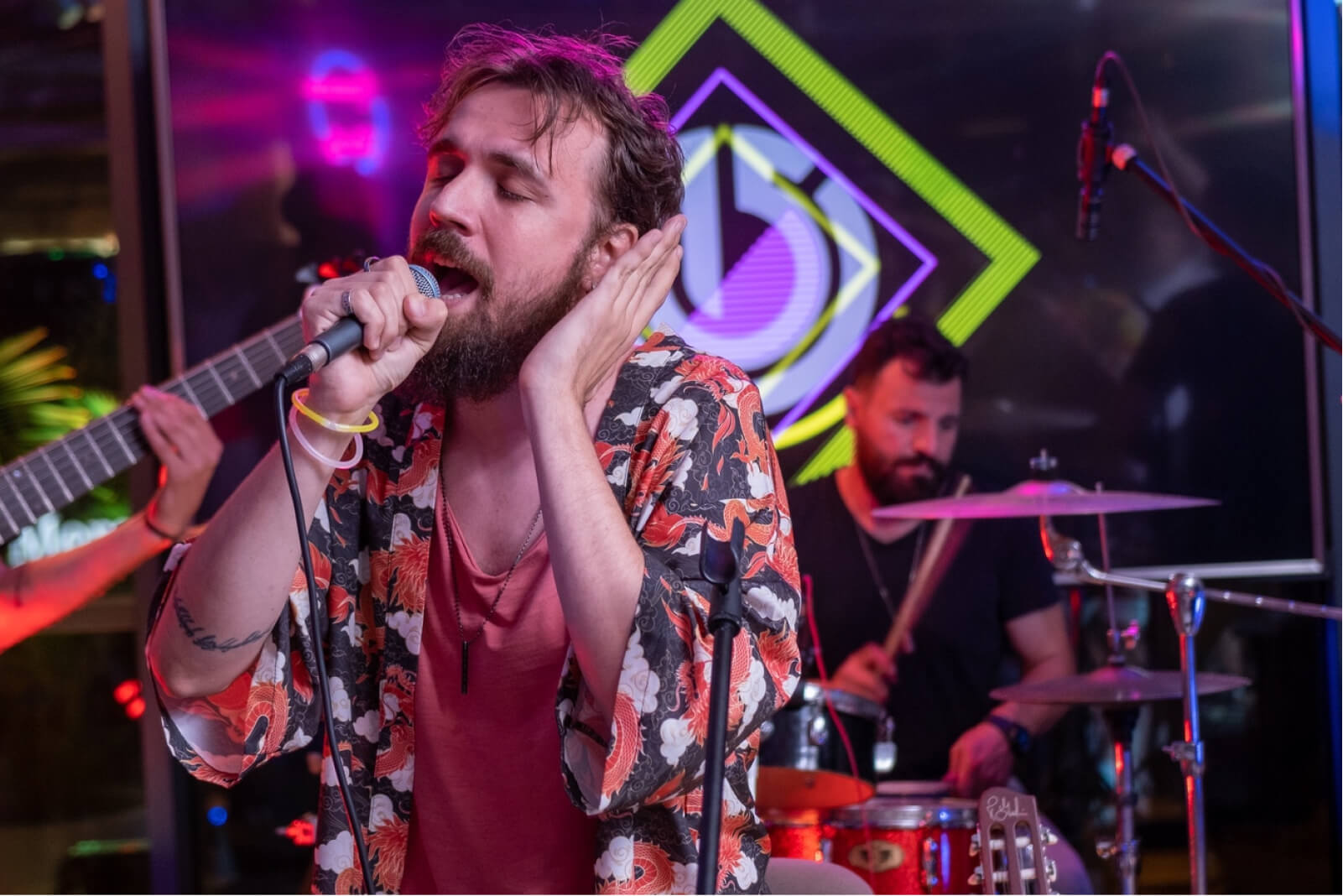 A bearded man singing into a microphone and a man playing the drums in front of the Atolye15 logo.