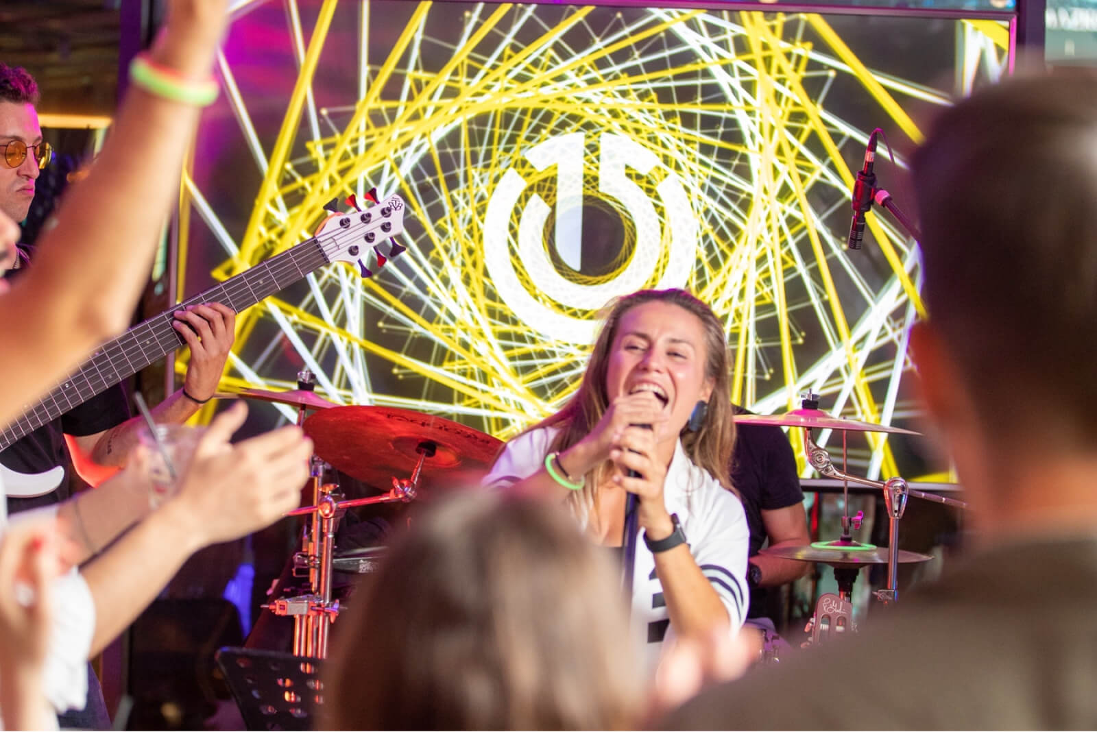 A woman singing into a microphone in a white t-shirt in front of the Atolye15 logo and people partying with their hands up.