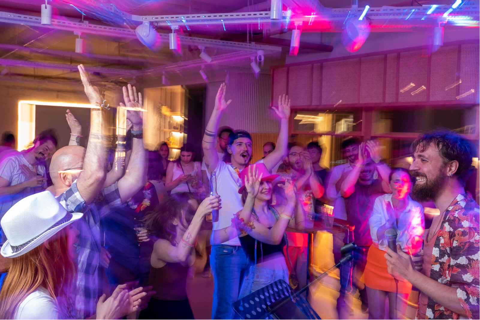 A group of people partying and dancing with their hands in the air and a male singer holding a microphone.