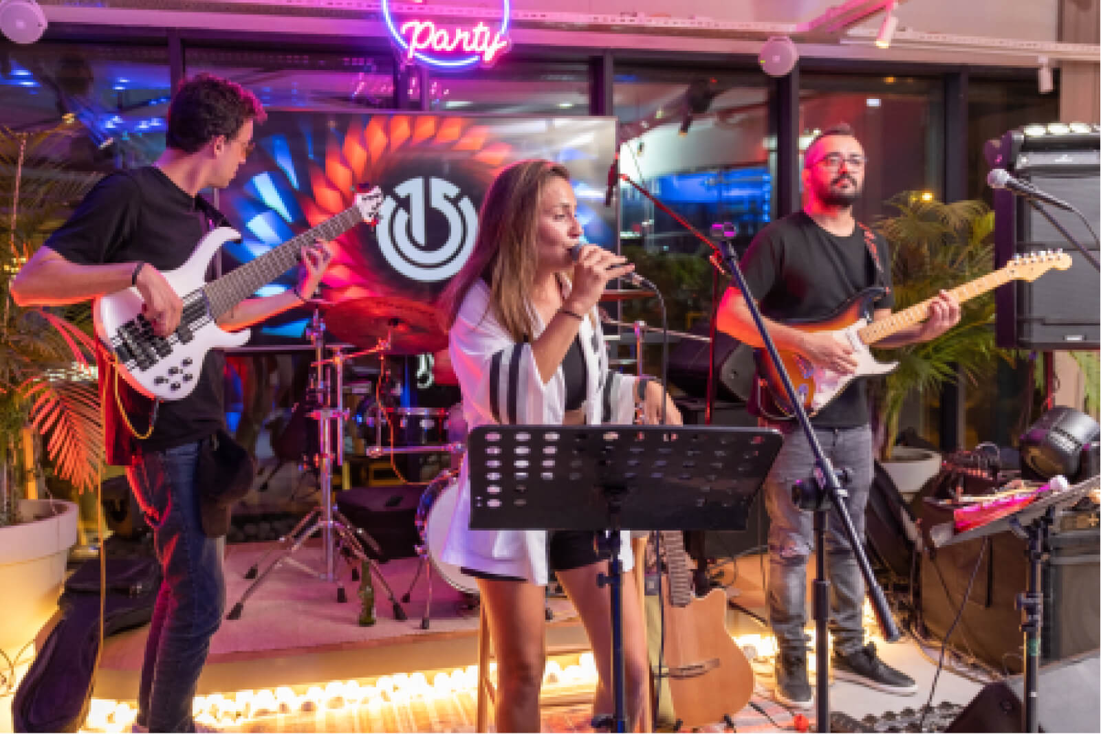 Two male guitarists and a female singer holding a microphone at a party in front of a screen that shows the Atolye15 logo.