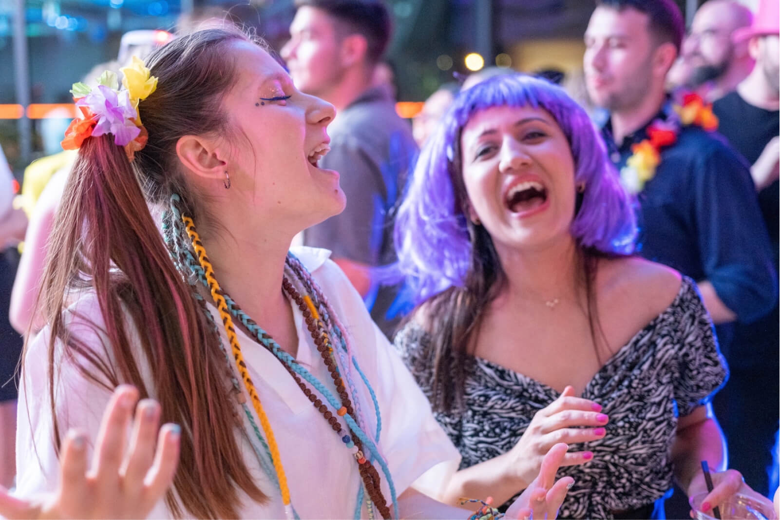 A young blonde girl with a colorful hair tie and and a woman wearing a purple wig singing together.
