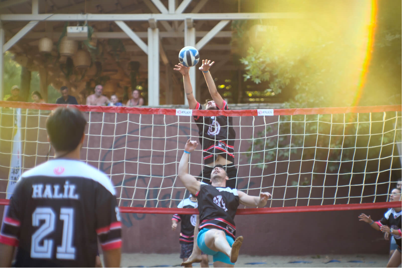 People jumping over the net to hit the ball while playing volleyball and a man wearing a jersey that says “Halil 21.”