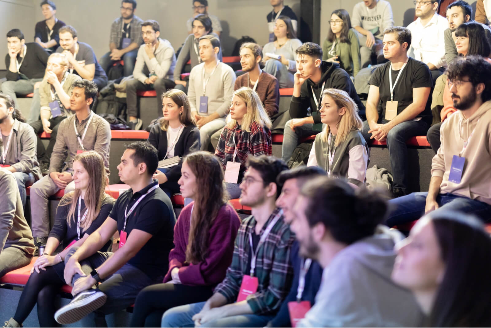 A crowd of people sitting in a lecture hall wearing Atolye15 intership bootcamp badge hangers around their necks.