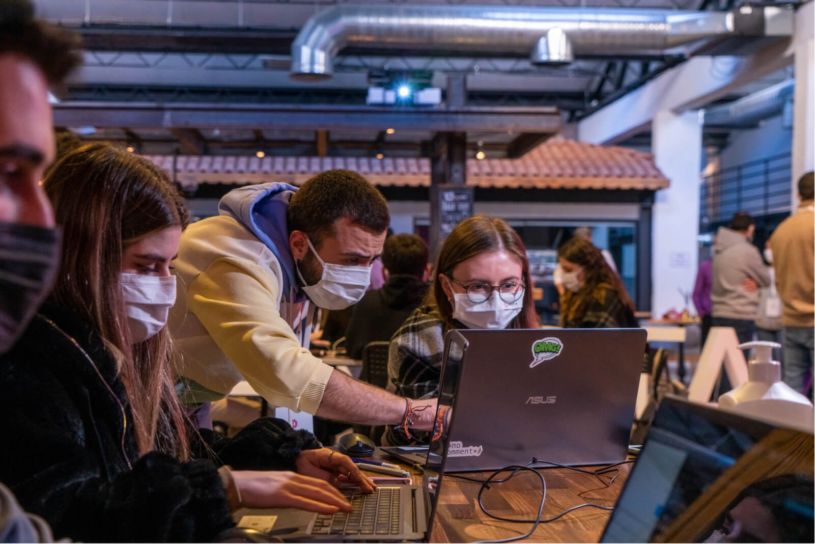 A man in a face mask and a hoodie pointing at a laptop and a young girl wearing glasses and a face mask.