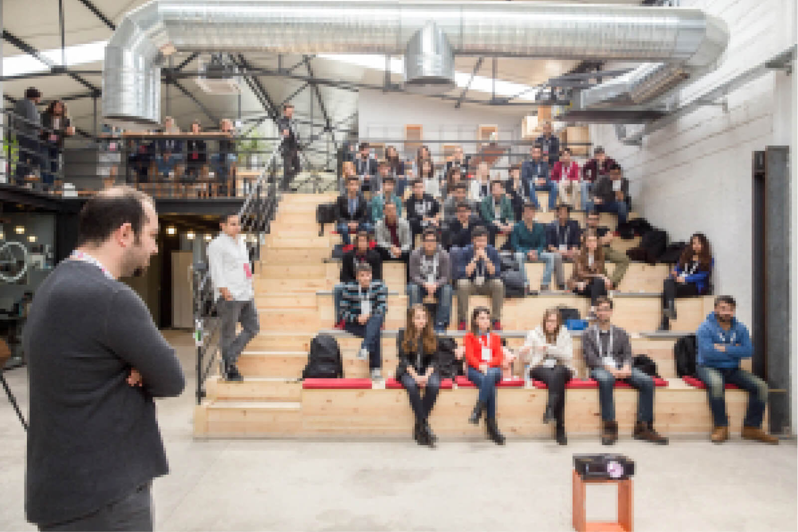 A man in a grey sweatshirt standing in front of a group of people sitting in a lecture hall at Atolye15’s 2nd Intern Bootcamp.