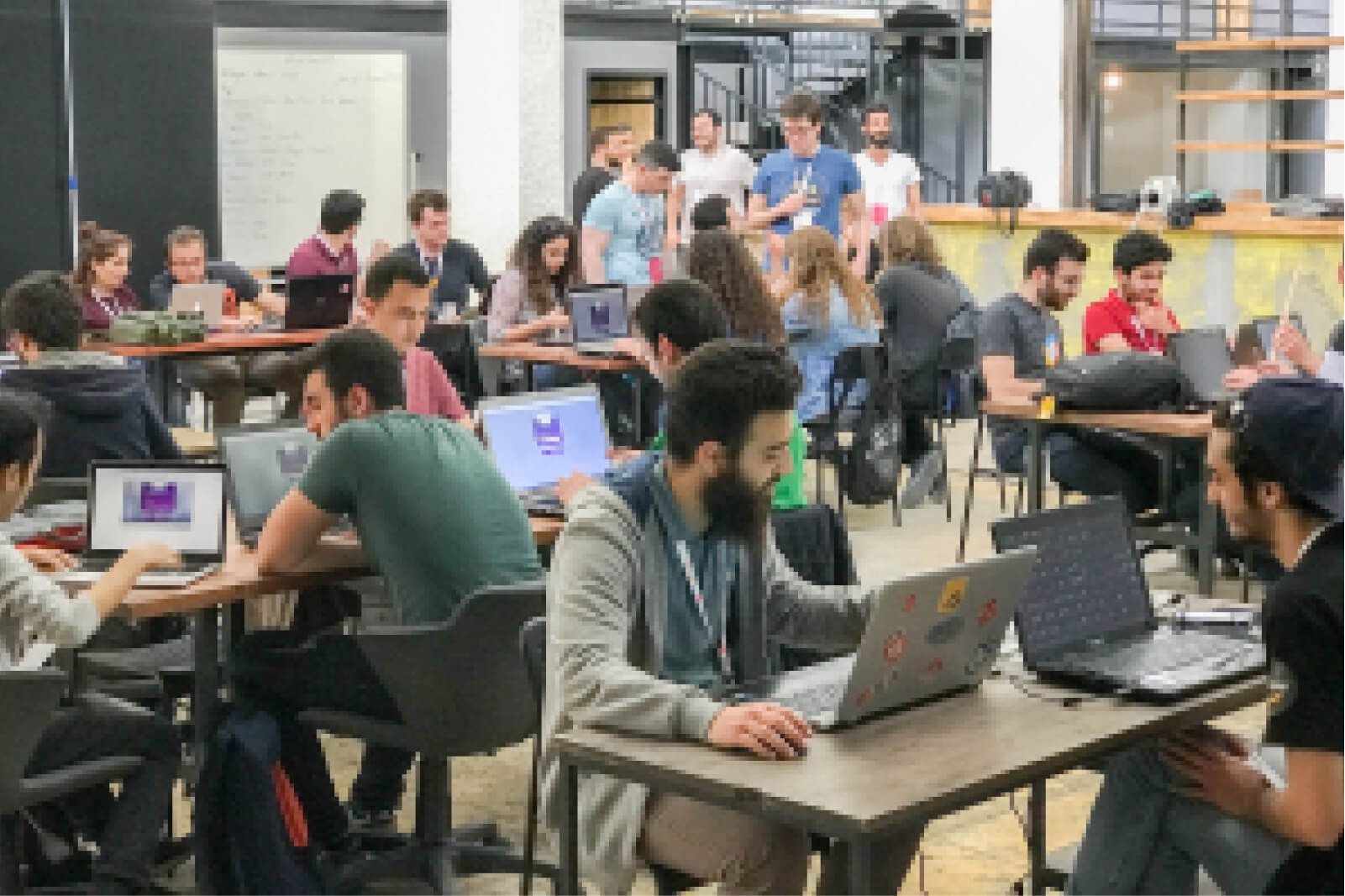 A group of young people working on their laptops, sitting around tables at the 3rd Atolye15 Internship Bootcamp.