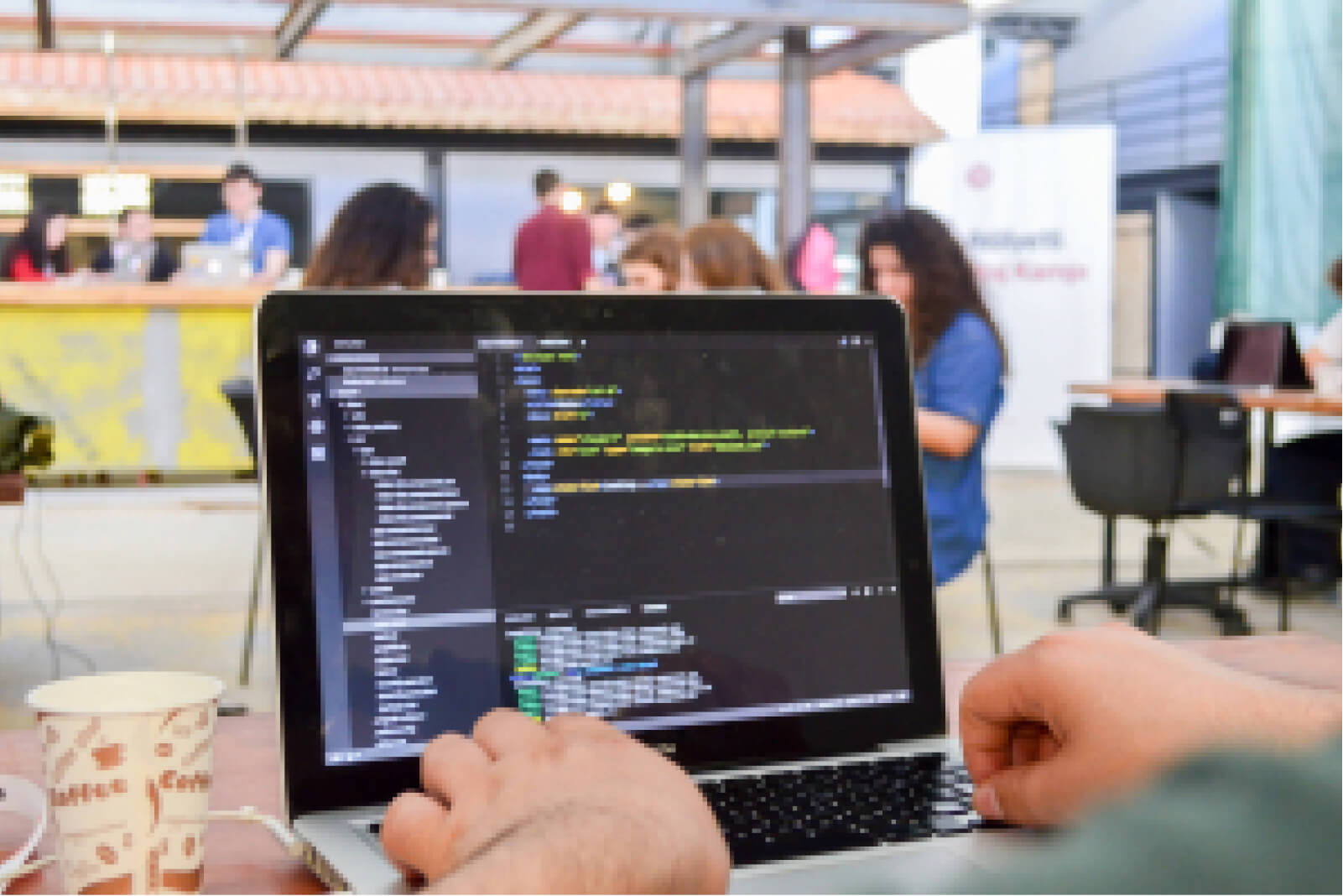 A laptop screen showing lines of code, a pair of hands on a keyboard, a cup of coffee, and an Atolye15 Staj Kampı banner.