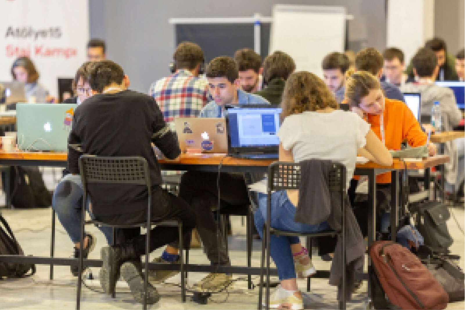 People sitting at tables across from each other, working on their laptops and an Atolye15 Staj Kampı banner.
