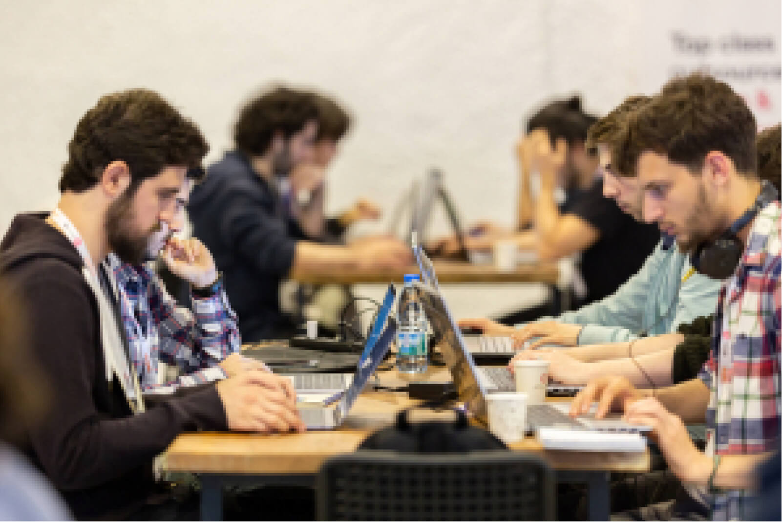A group of young men sitting across tables and working on their laptops.