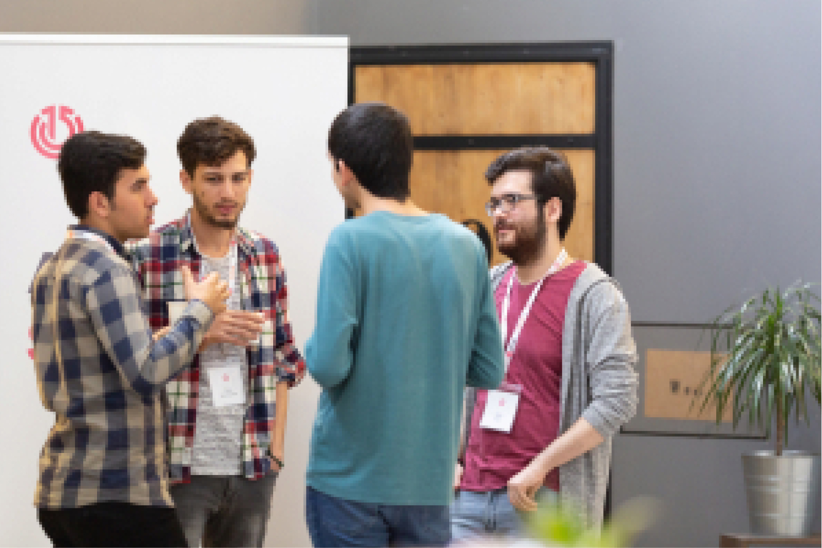 Four young men talking to each other gathered in front of a banner with the Atolye15 logo on it.