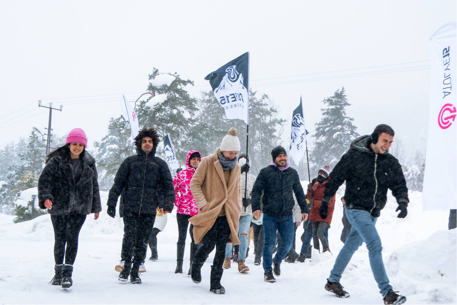 A group of people walking in the snow wearing winter coats and hats, and winter retreat banners with the Atolye15 logo on them.