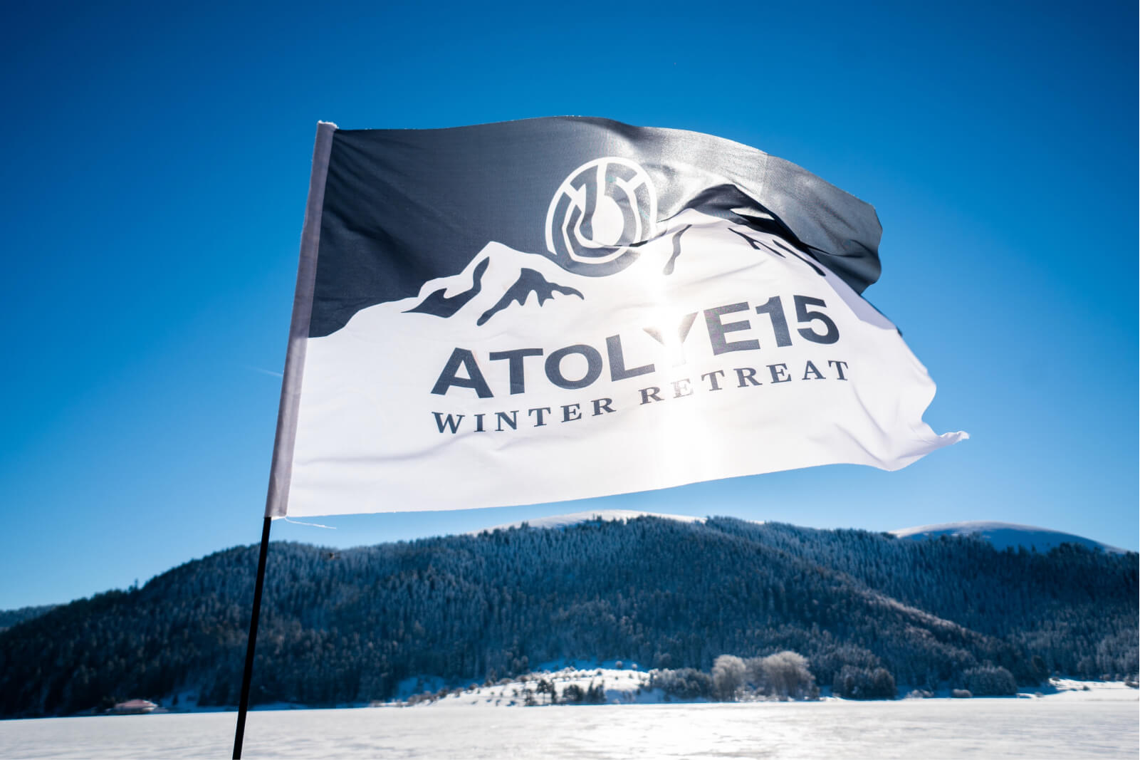 A waving flag that says “Atolye15 Winter Retreat” in front of a mountain of pine trees and a snowy landscape.