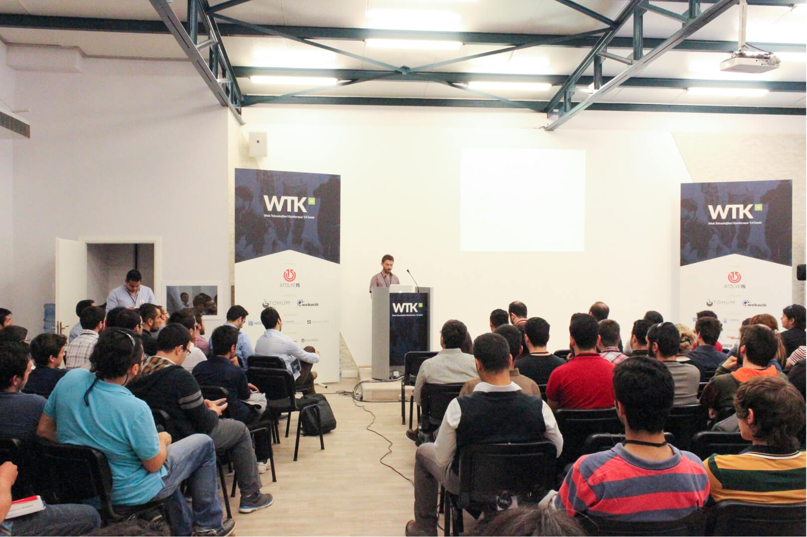 A man at a lectern giving a speech in front of a crowd of people sitting in a conference hall at Atolye15’s WTK.