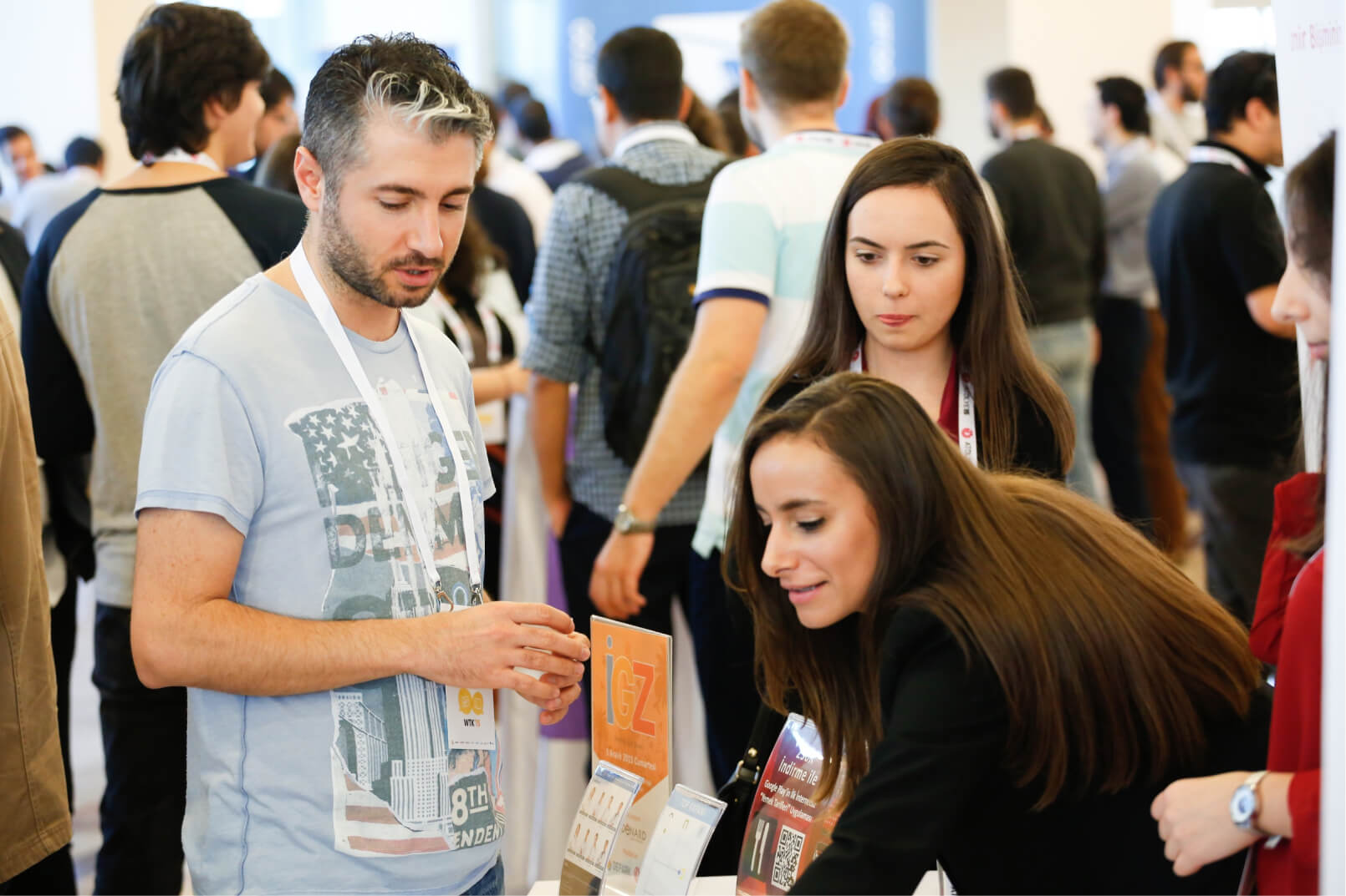 A man in a blue t-shirt, a long-haired woman, and another young woman in front of a crowded background at WTK’15.