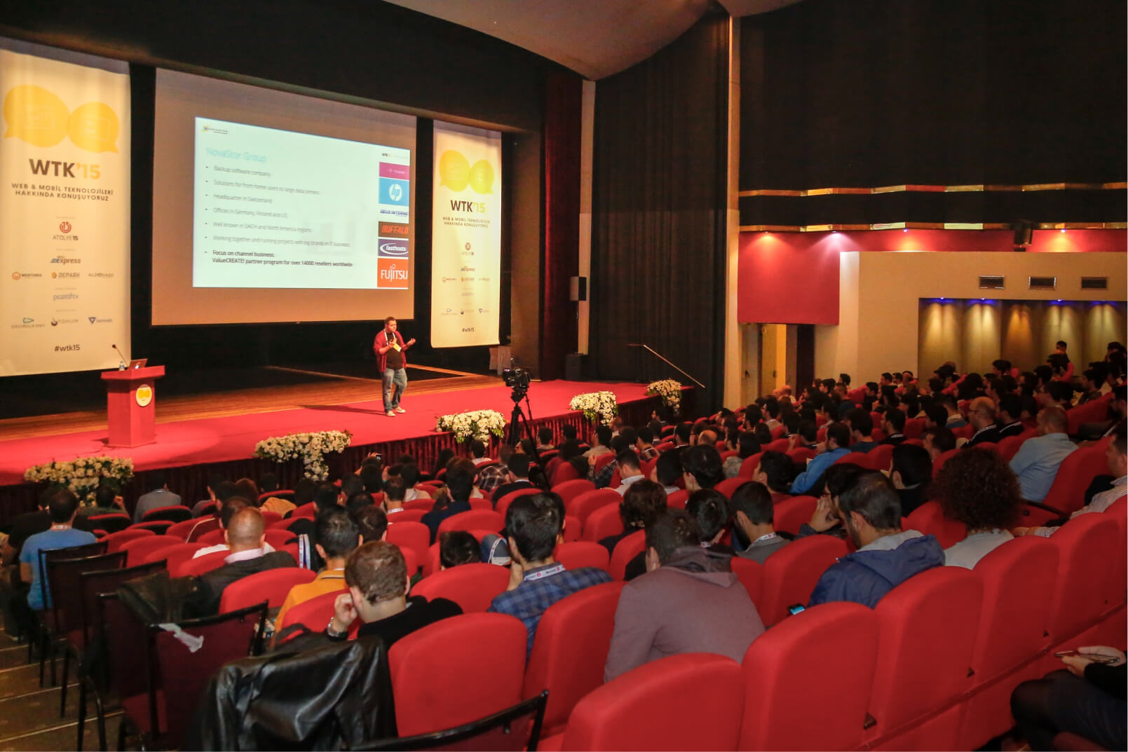 A man on a red stage at a conference hall giving a speech to a crowd of people at Atolye15’s WTK in 2015.