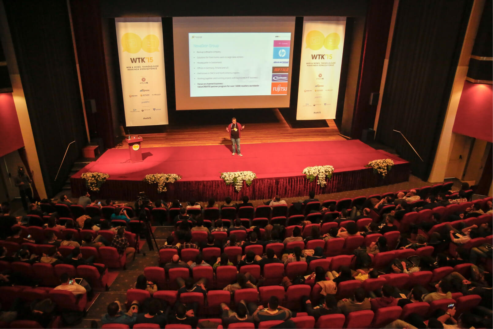 A man on a red stage at a conference hall giving a speech to a crowd of people at Atolye15’s WTK in 2015.