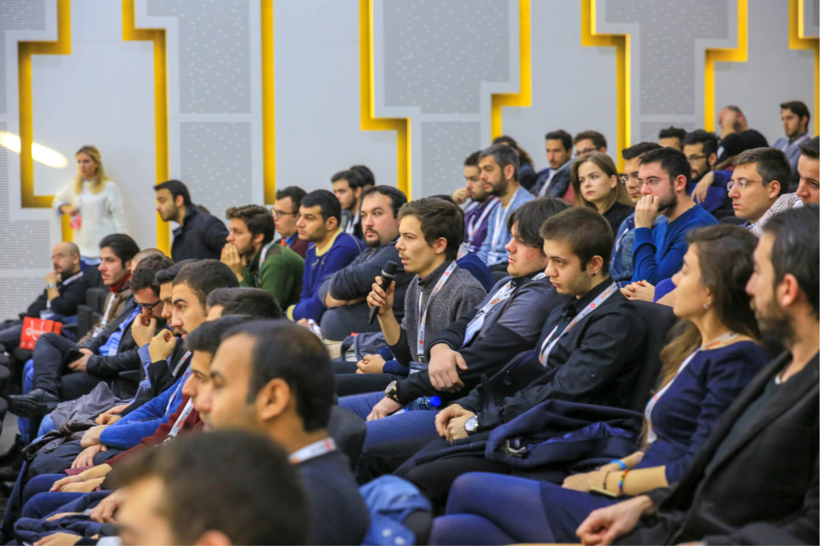 A young man sitting among a crowd at the WTK’16 tech conference and talking into a microphone.