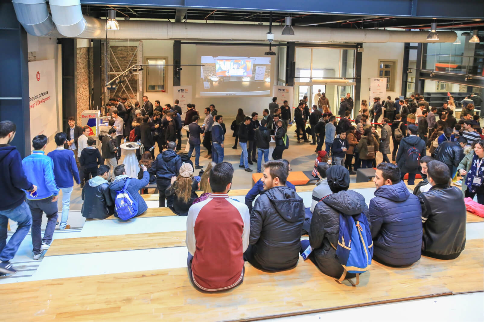 A group of people standing and sitting around talking and networking at the WTK’16 tech conference by Atolye15.
