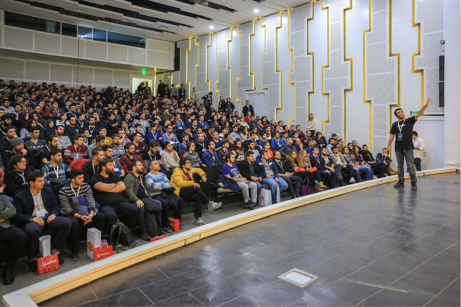 A man on stage pointing at something and giving a presentation in front of a big crowd of people in the WTK’16 conference hall.