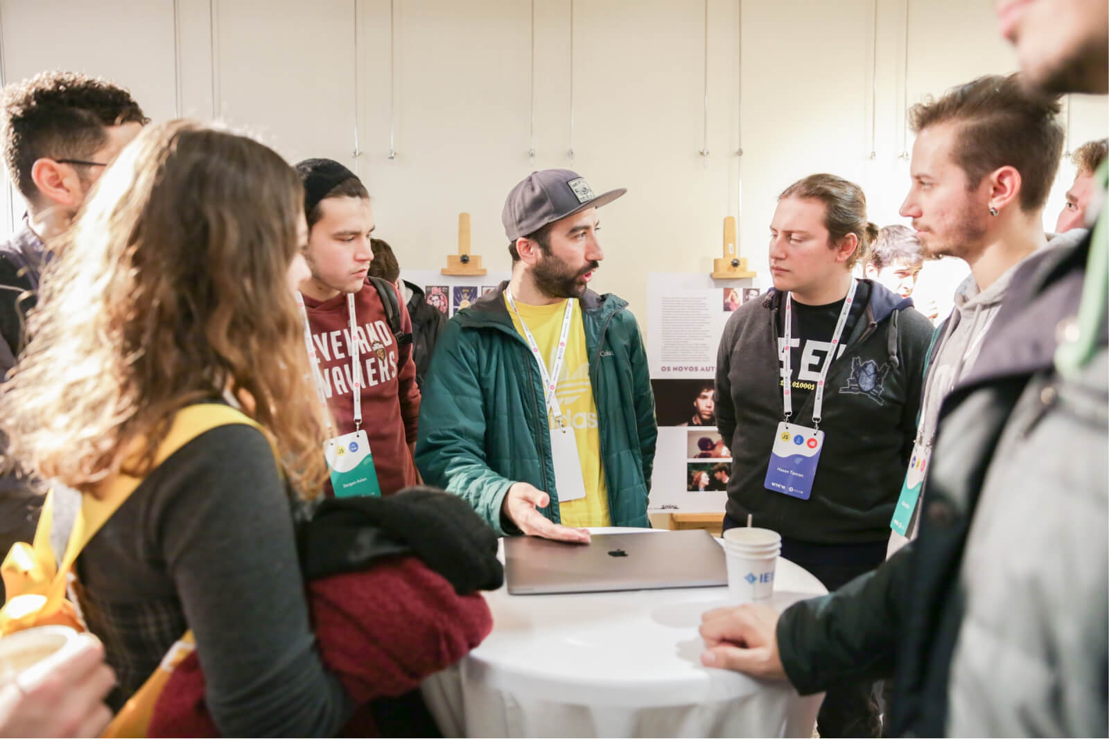 A group of young people gathered around a table with a MacBook, having a conversation.