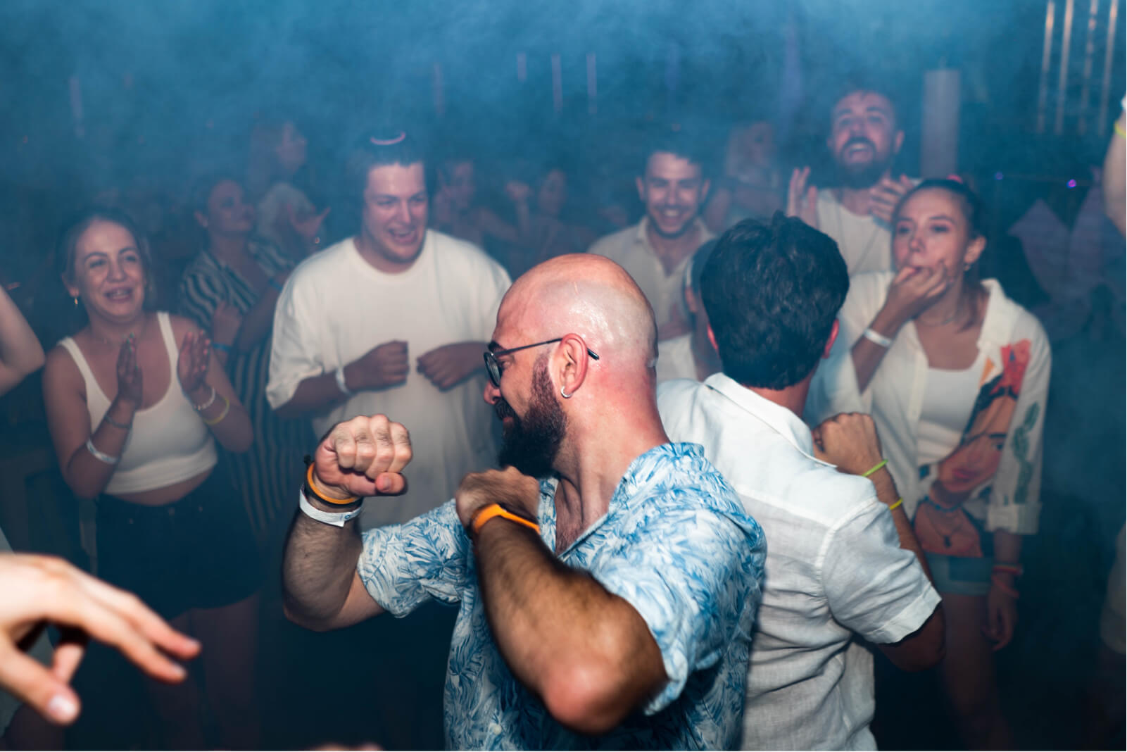 A group of people partying and dancing on a dancefloor covered with smoke.