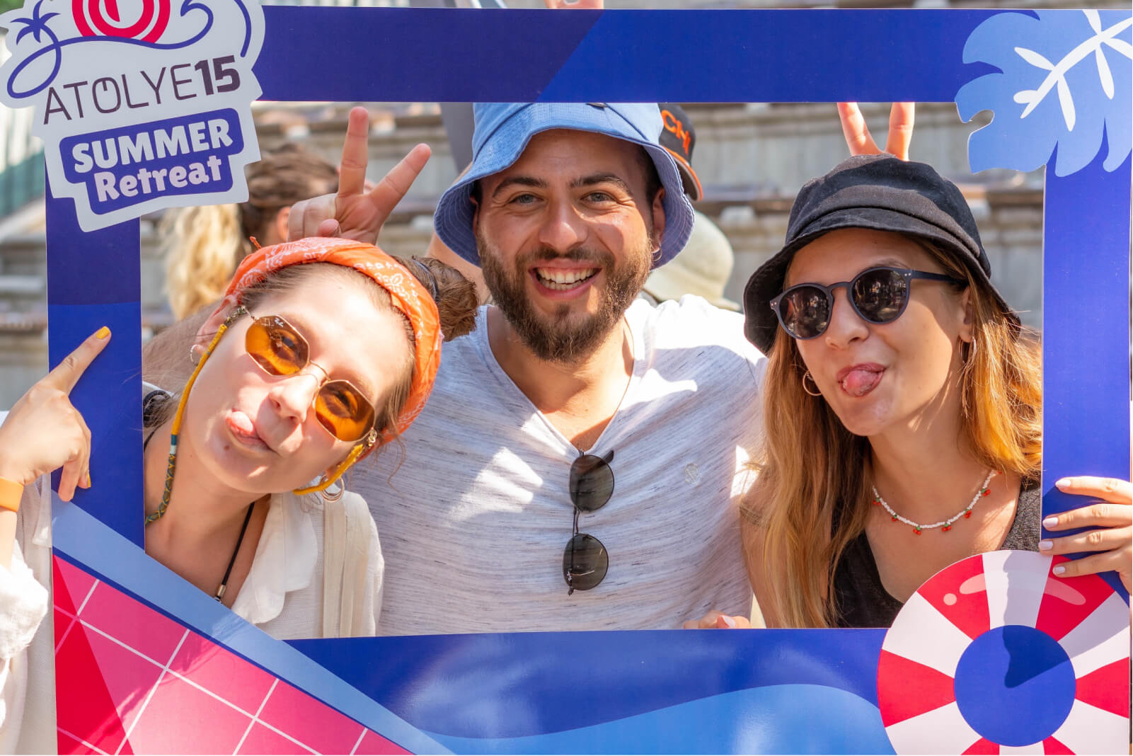 Two women wearing sunglasses and sticking their tongues out and a man in a blue hat holding an Atolye15 Summer Retreat frame.