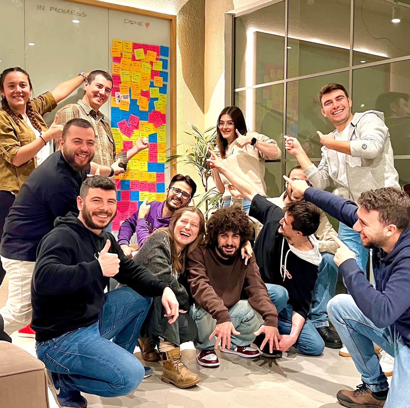 Team members of Atolye15 gathered in front of a task board, smiling and pointing at the completed tasks they have accomplished for Heinrich Schmid.