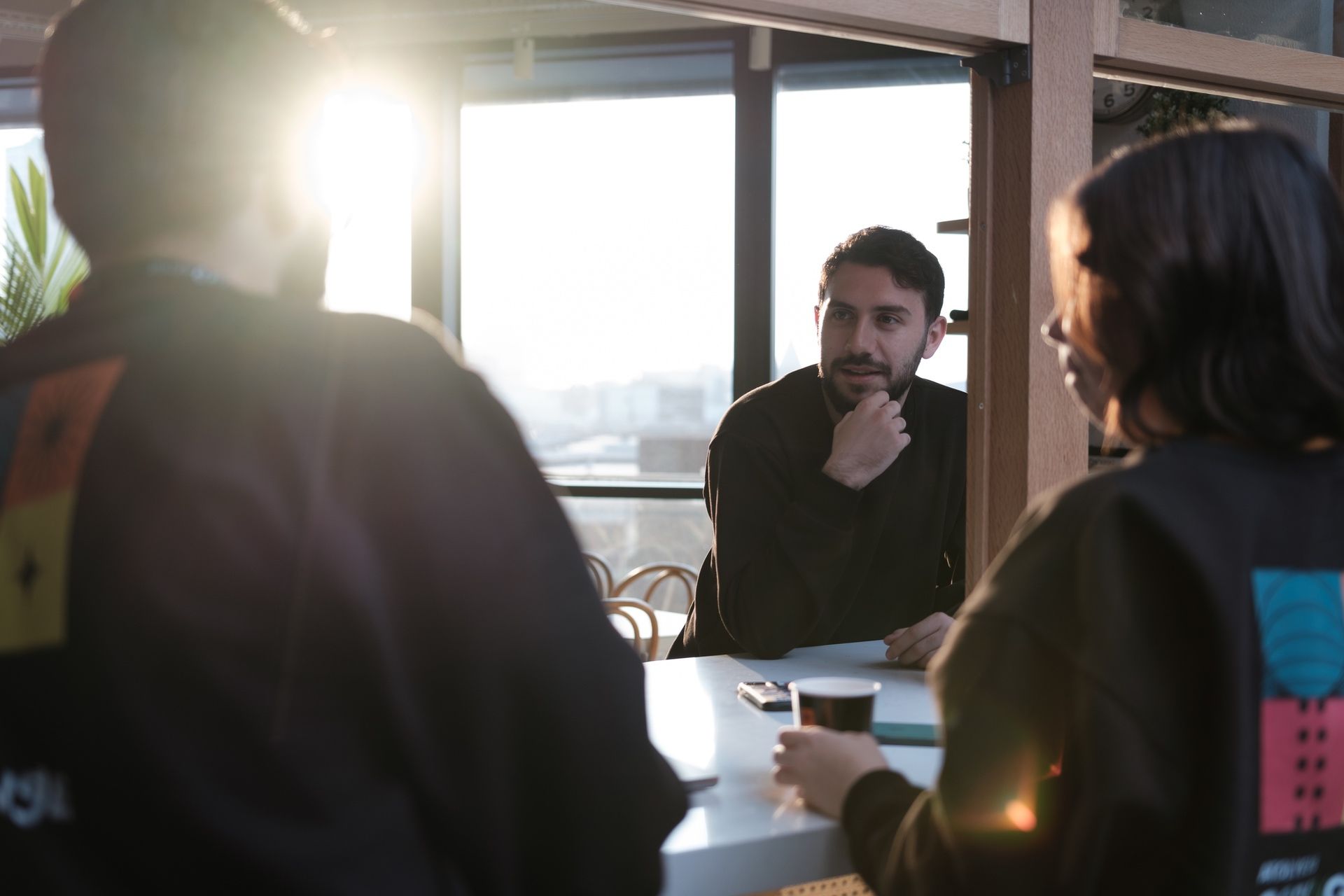 Three people in the Atolye15 İzmir office, two facing away and one in the foreground wearing Coding Challenge sweatshirts, engaged in conversation.