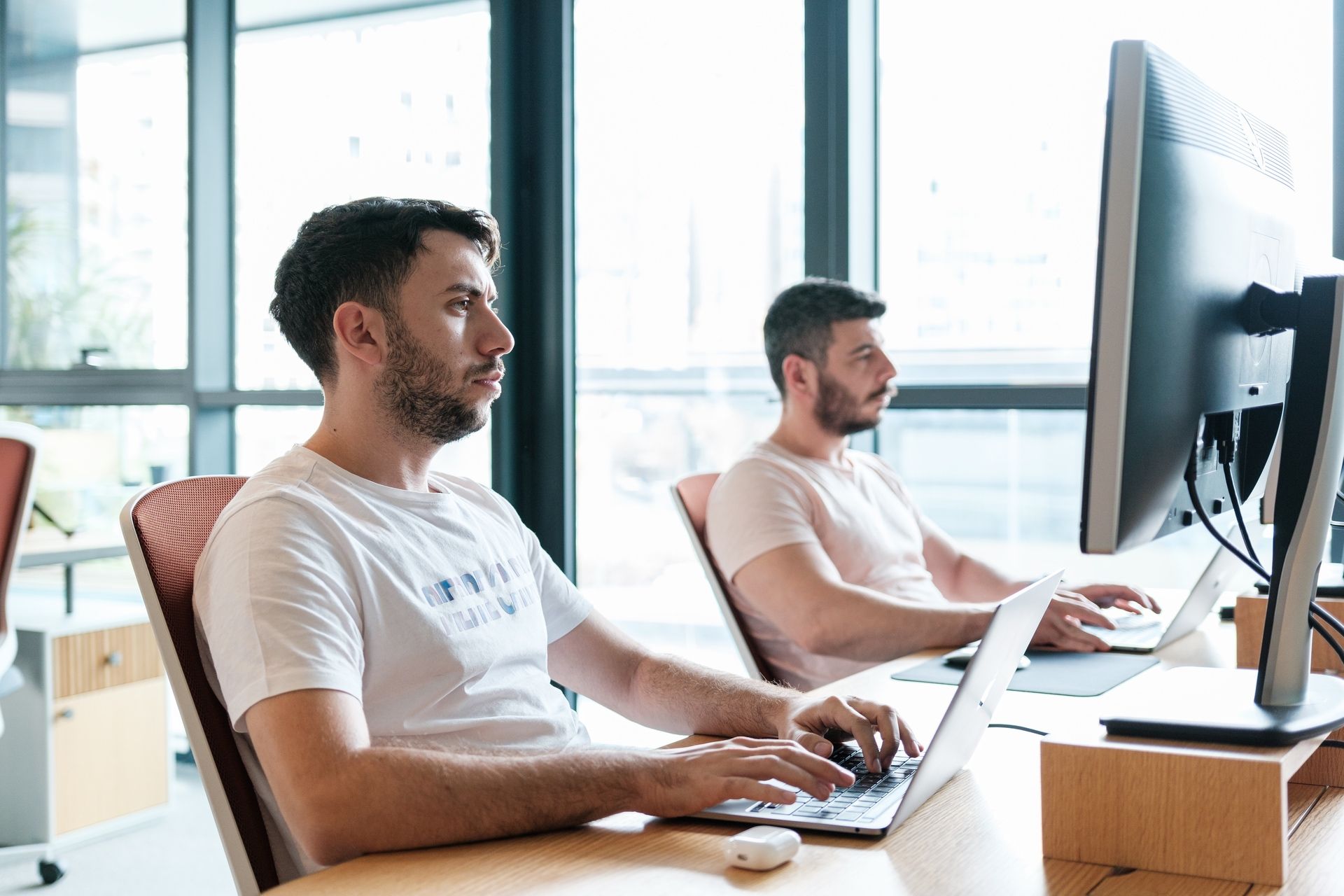 Atolye15 developers Alperen Türköz and Hasan Aydoğdu wearing white t-shirts and writing code at the office desks.