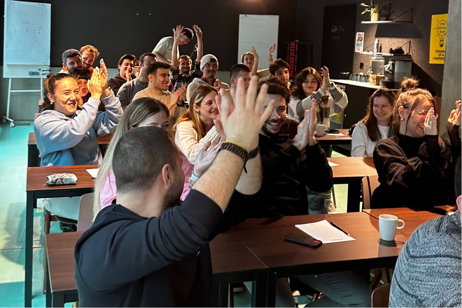 The Atolye15 Team sitting in a meeting room, smiling, and clapping with their hands in the air during kickoff.