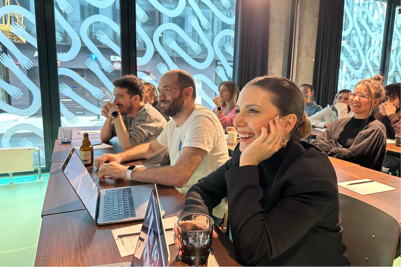 A group of Atolye15 Team members sitting on wooden desks in front of their laptops and smiling during the kickoff meeting.