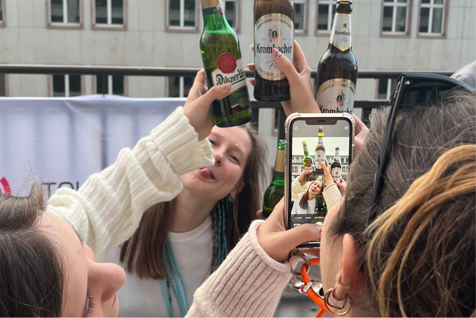 A group of female Atolye15 employees holding German beers and posing for a picture taken by an iPhone on the Berlin office terrace.