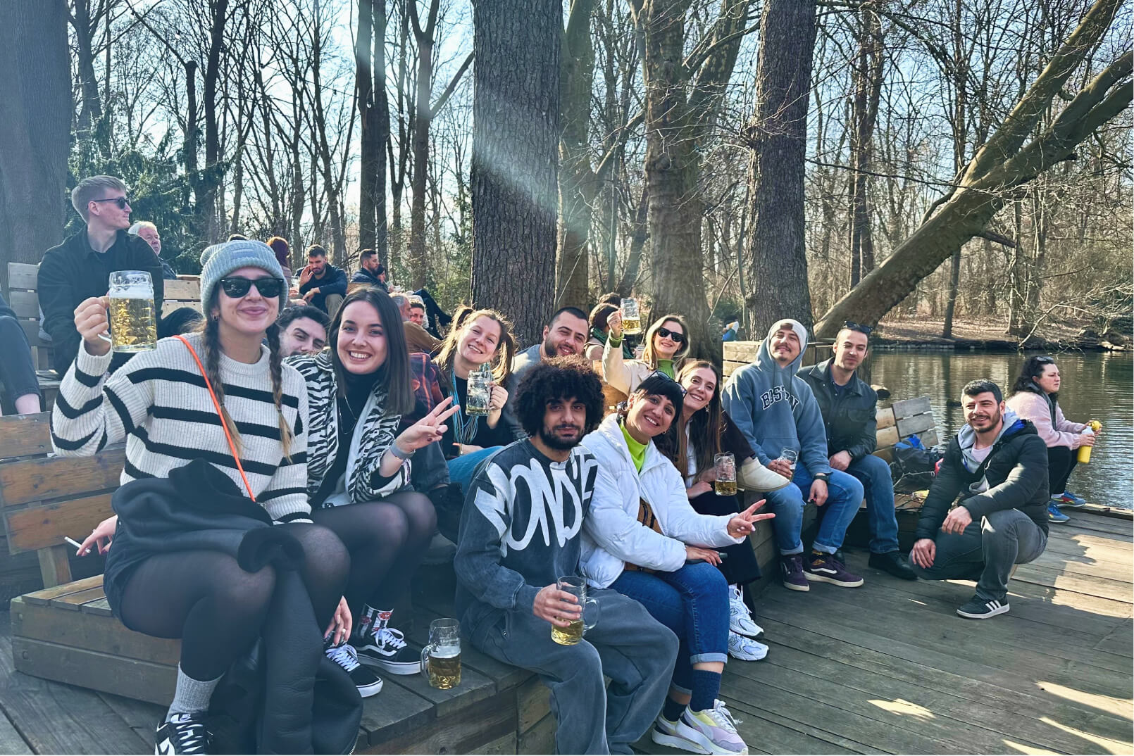 A group of Atolye15 employees in the woods, sitting by a lake and raising beer glasses in a Biergarten in Berlin.