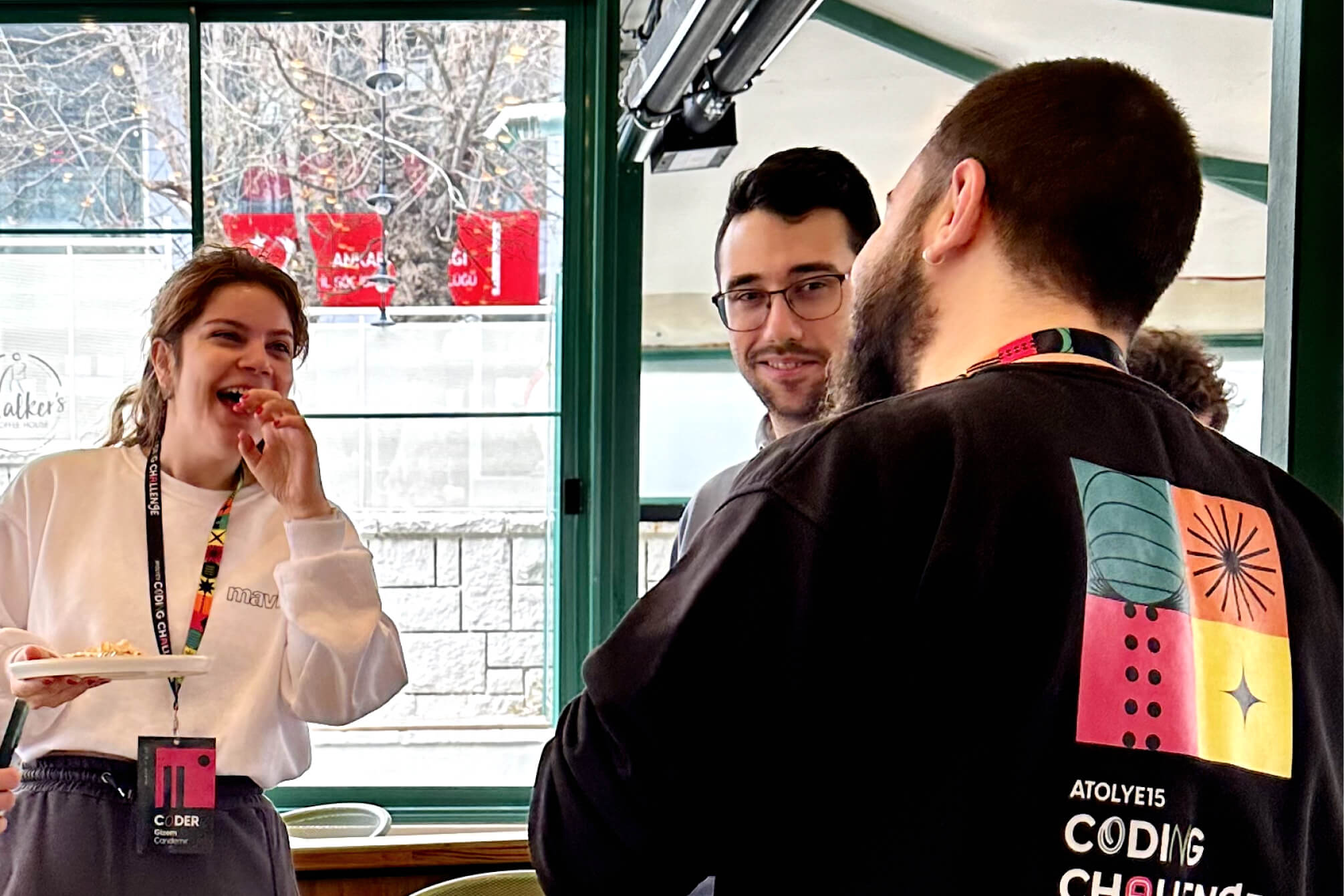 A young woman wearing a pink name tag, laughing, and having a conversation with an Atolye15 team member wearing a Coding Challenge sweater.