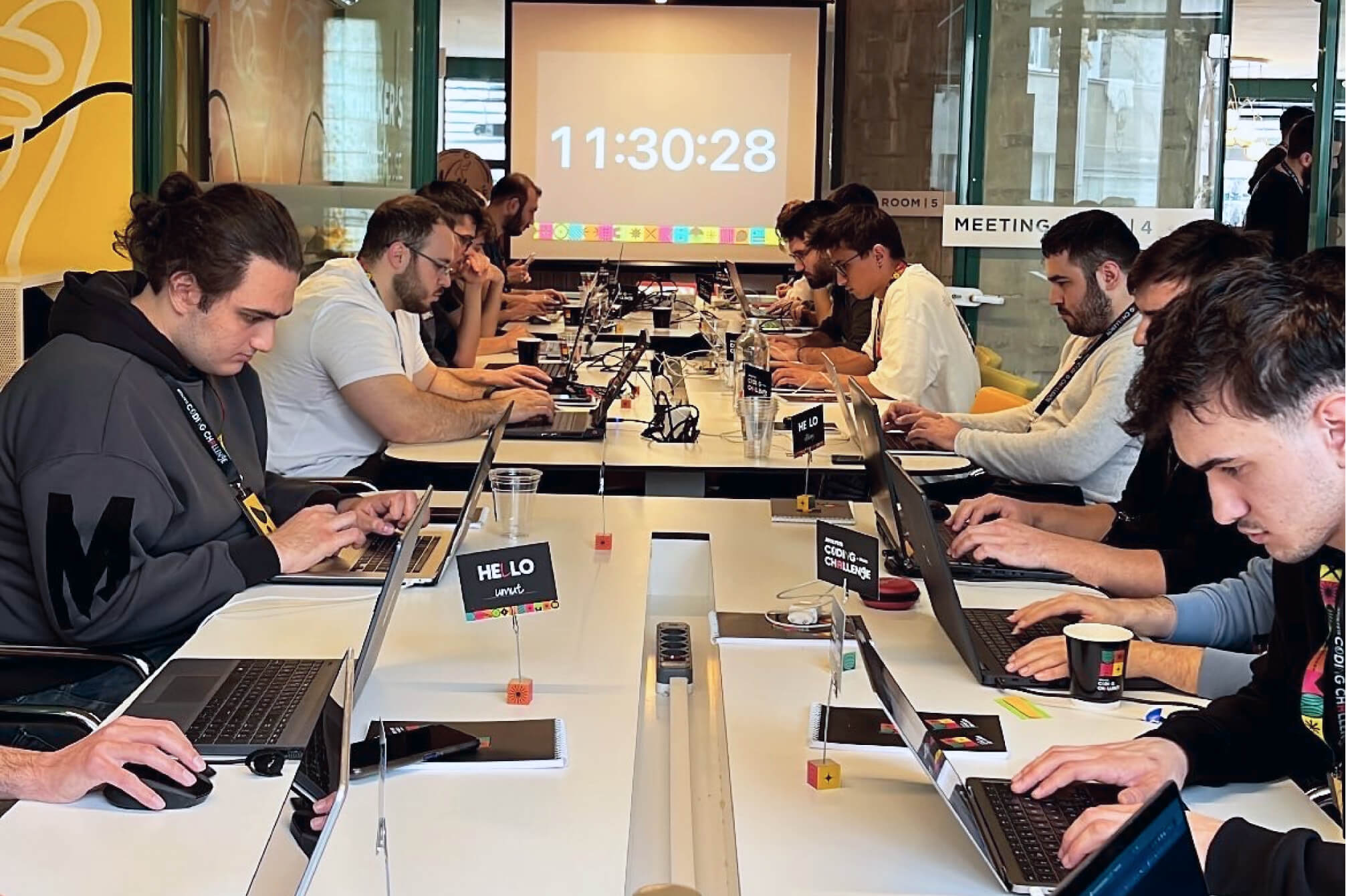 Atolye15 Coding Challenge Ankara participants gathered around a desk, coding on their laptops with a countdown screen in the background.