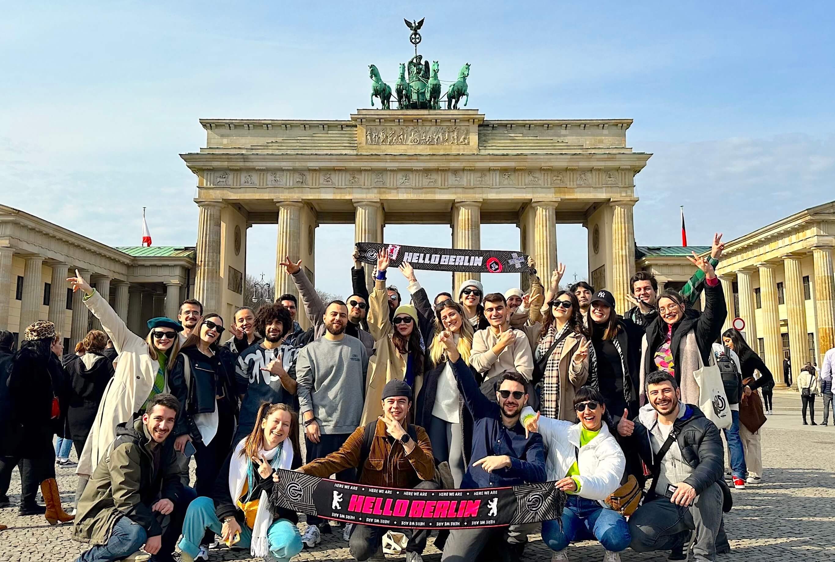Atolye15 employees holding “Hello Berlin”' scarfs in front of Brandenburg Gate.