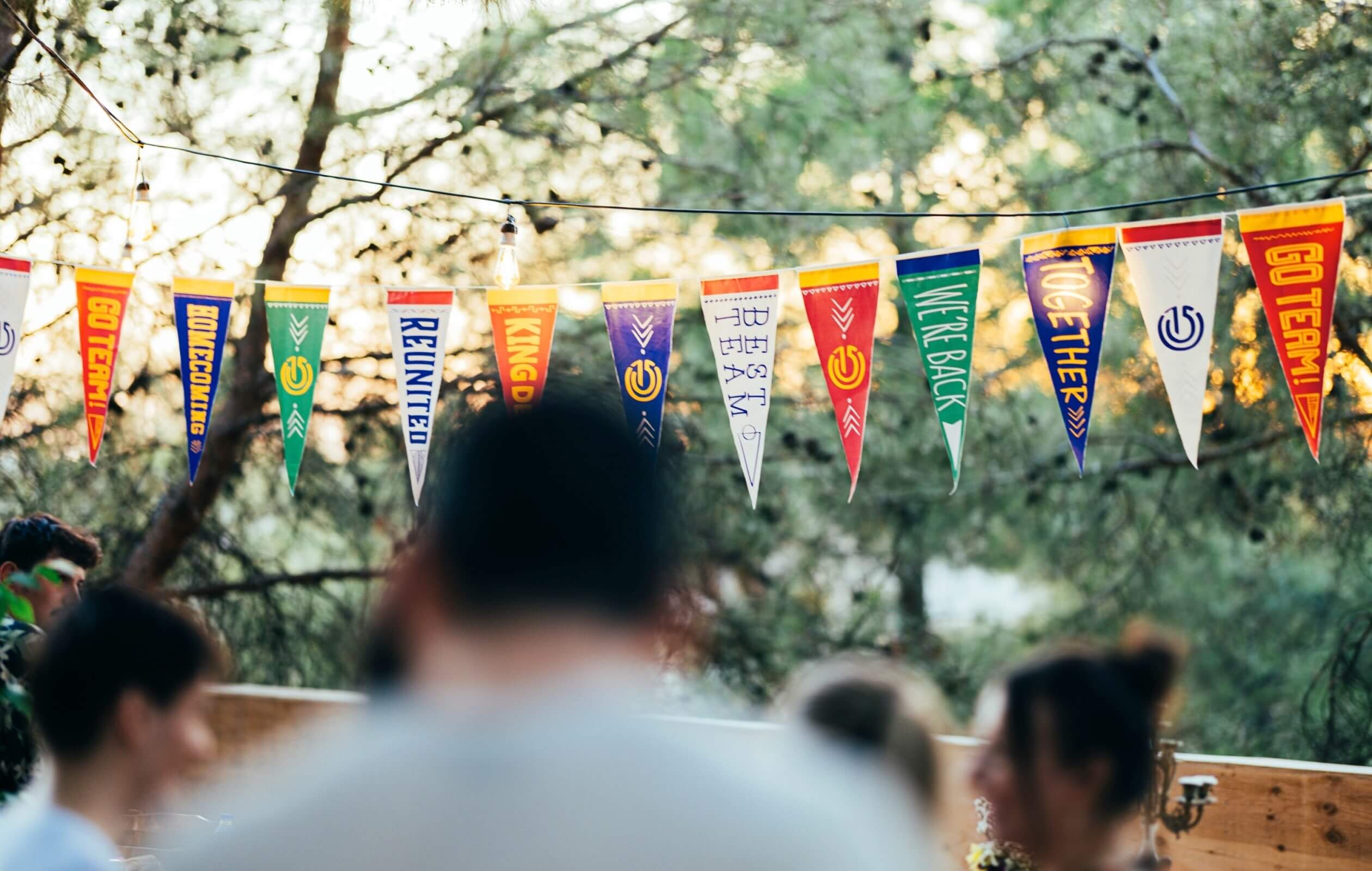A line of colorful pennant flags strung together, displaying messages such as 'We're Back,' 'Reunited,' 'Homecoming,' and 'Best Team,' along with the Atolye15 logo.