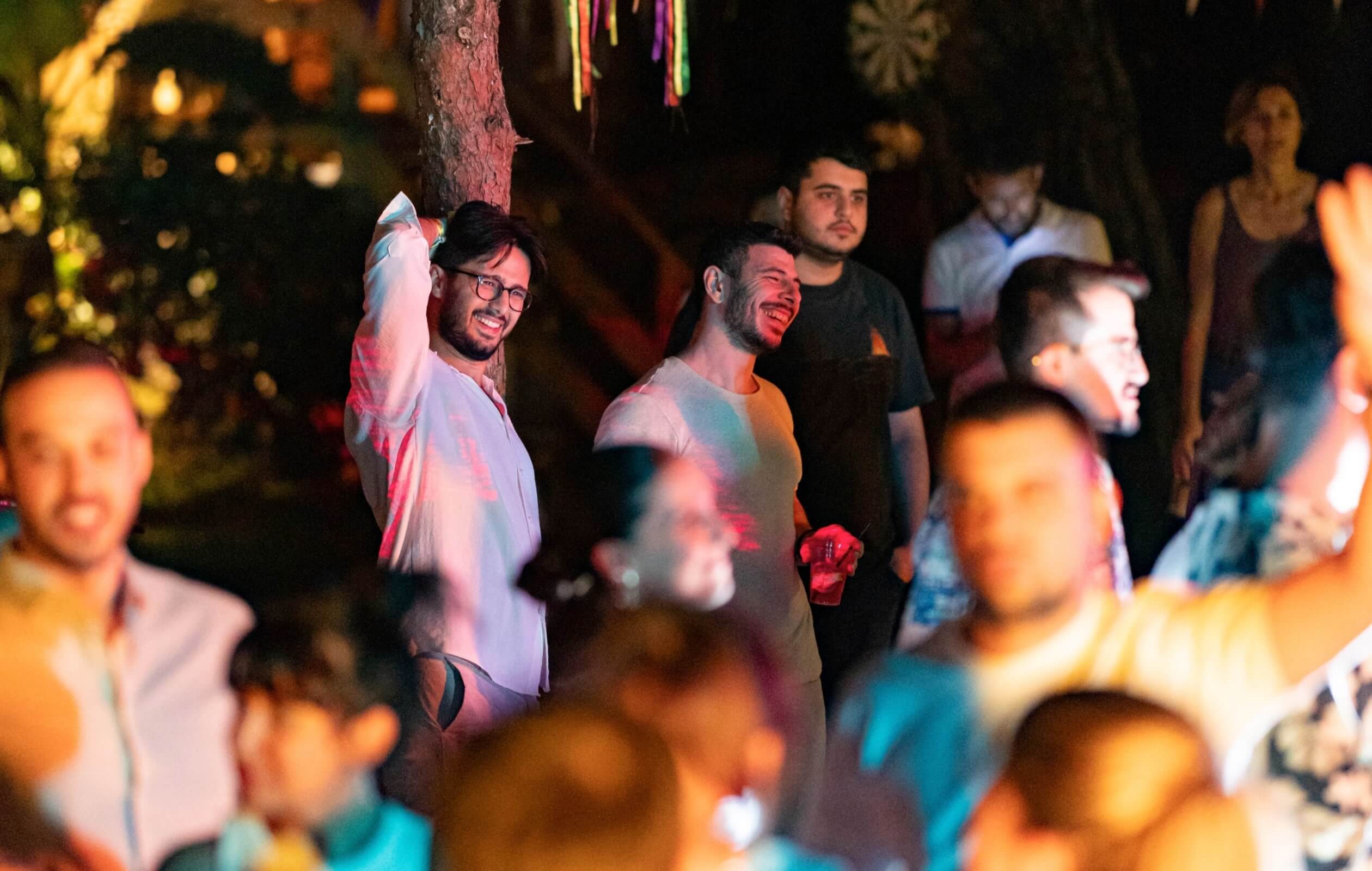 A group of people smiling and dancing under trees decorated with Atolye15 Homecoming pennant flags during a concert.
